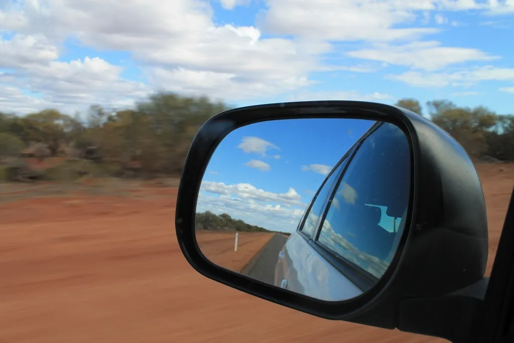 A red dirt road seen in a car's side mirror